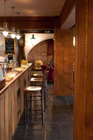 Un espace bar avec un comptoir en bois, des tabourets et des luminaires suspendus.