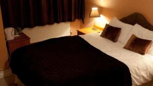 Une chambre d’hôtel avec un lit, une table de chevet, une lampe et une fenêtre avec des rideaux.