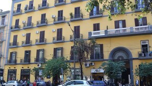 Un edificio amarillo de varios pisos con balcones, una tienda con un letrero que dice "Aké" y coches estacionados a lo largo de la calle.