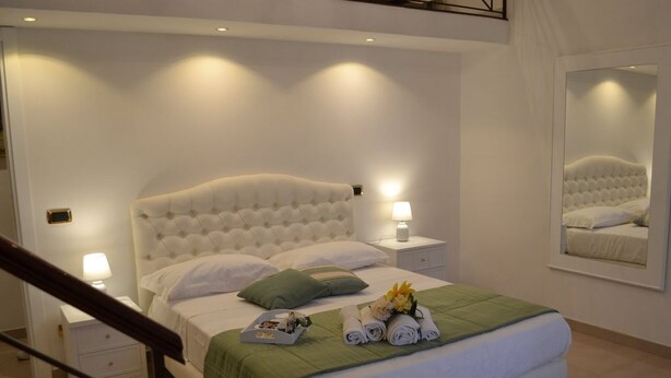 Una cama bien hecha con un edredón verde, dos lámparas de noche y un espejo en la pared.