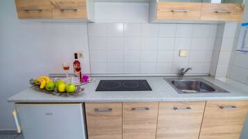 Een koelkast, een waterkoker, kookgerei, borden en bestek, eettafels
