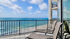 A balcony with two chairs, a view of the ocean, and a beach with umbrellas. - The Oasis 1209 | Spacious! Lazy River, Pool Slide, Poolside Grill! (Orange Beach)