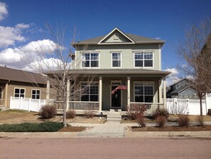 A two-story house with a front porch, a flag, and a picket fence.