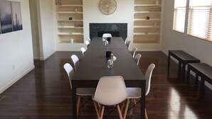Une salle à manger avec une longue table, des chaises blanches et des étagères ornées d’objets décoratifs.