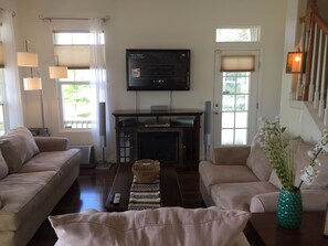 A living room with two beige sofas, a television mounted on the wall, a fireplace, and a decorative vase with flowers.