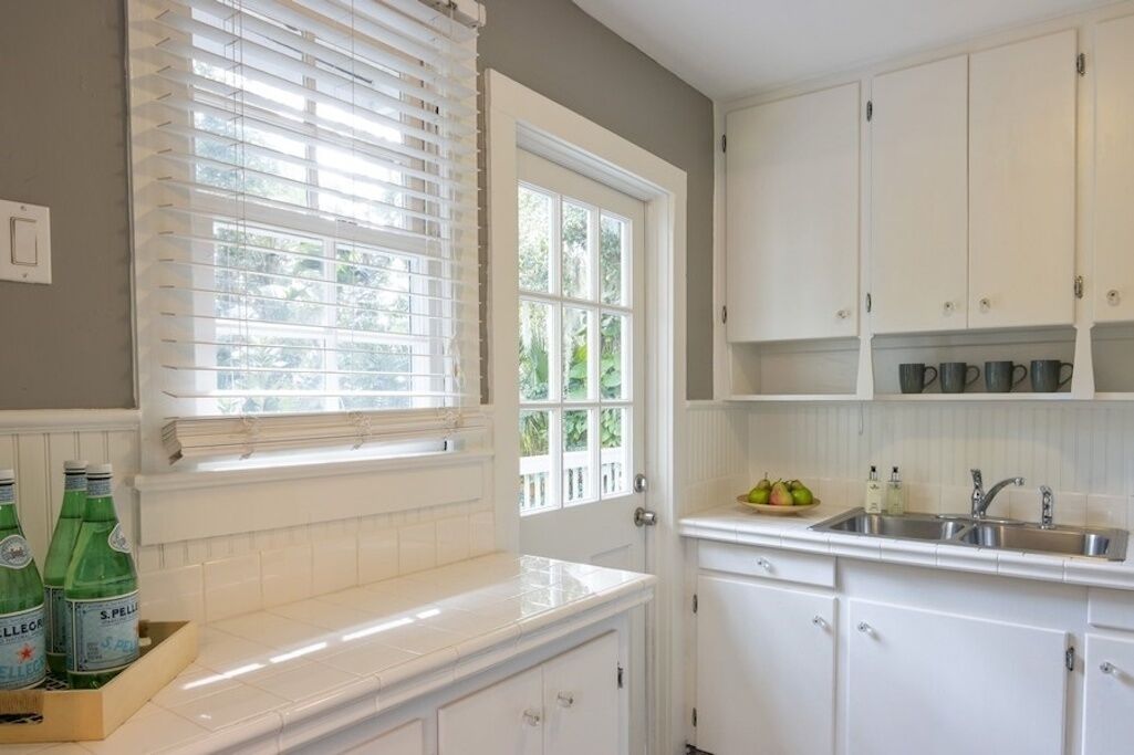 A kitchen with white cabinets, a window with blinds, and a countertop with bottles.