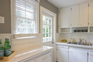 A kitchen with white cabinets, a window with blinds, and a countertop with bottles. - Windsor Bungalow Retreat- come for work and relaxation (Sarasota)