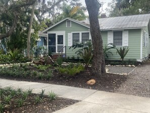 A green house with a porch, surrounded by various plants and a tree. - Windsor Bungalow Retreat- come for work and relaxation (Sarasota)