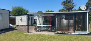 A mobile home with a patio area featuring a table and chairs, a fenced enclosure, and a satellite dish.