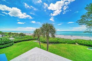 A beach view with a clear sky, palm trees, and a grassy area with a bench. - Unit #318 Sand Cay Beach Resort Gulf Front (Longboat Key)