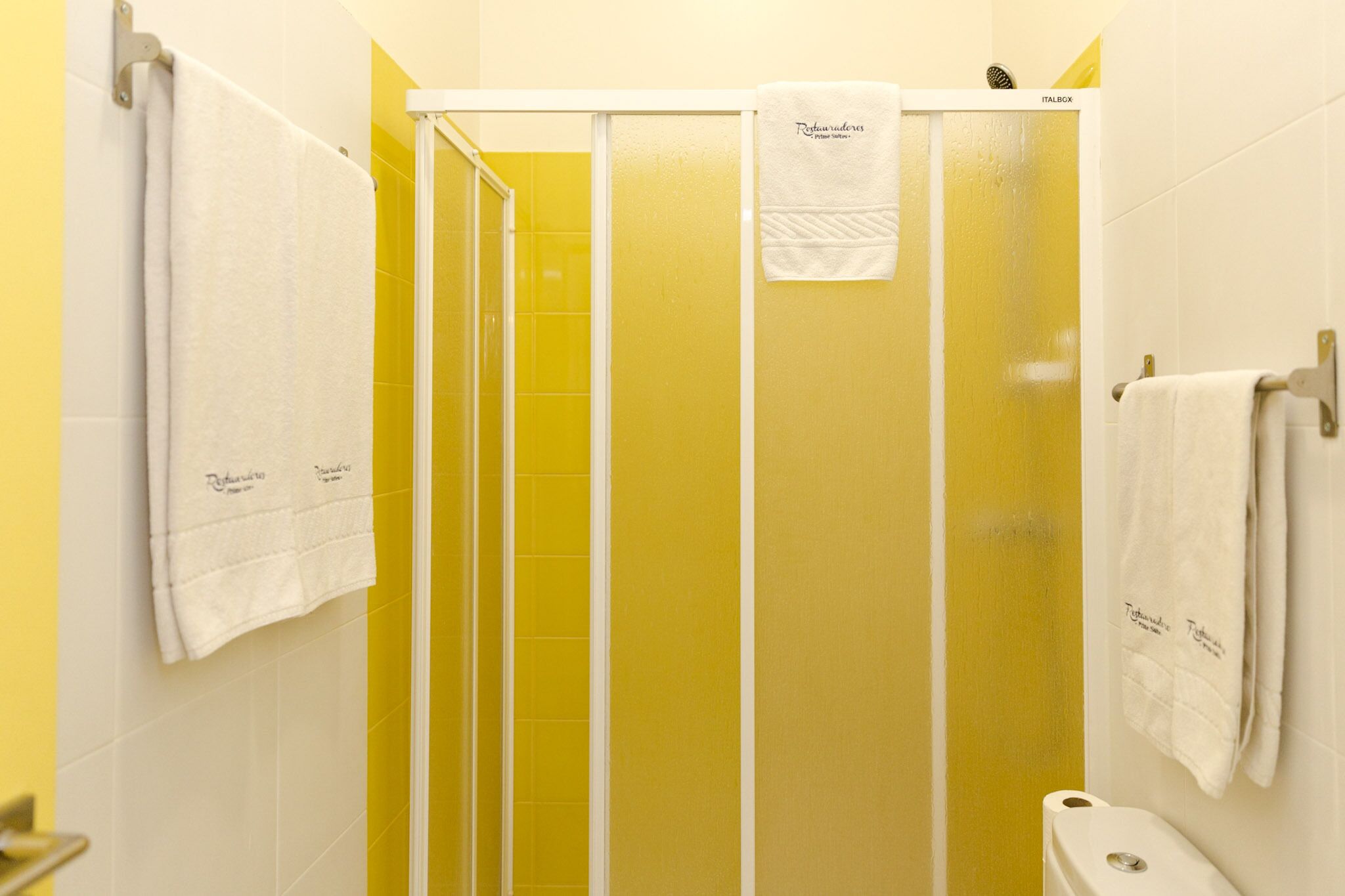 A bathroom with yellow walls, a white bathtub, and two white towels hanging on the wall.