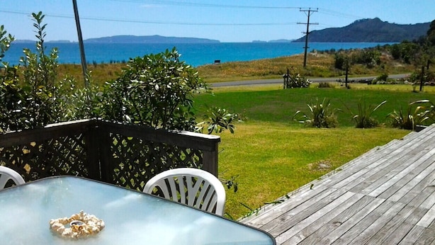Ein Glastisch mit einer Popcornschale auf einer Holzterrasse, mit Blick auf ein Wiesenfeld und ein Gewässer in der Ferne.
