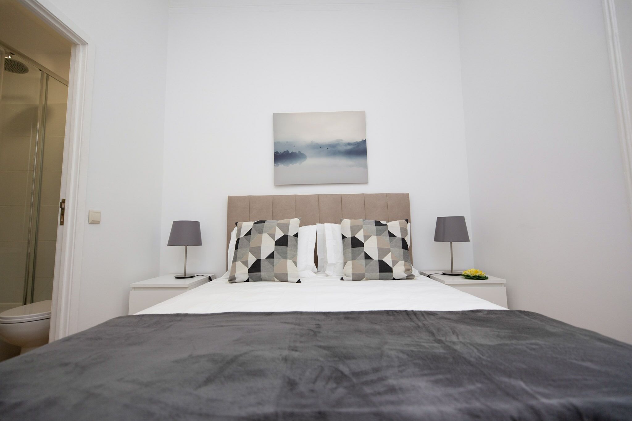 Une chambre à coucher comprenant un lit, deux tables de chevet, une commode, une œuvre d’art accrochée au mur et un espace douche.
