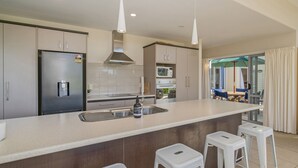 Une cuisine moderne dotée d’appareils électroménagers en acier inoxydable, d’un îlot central avec des tabourets et donnant sur un espace de détente extérieur.