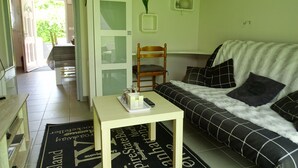 Una sala de estar con un sofá, una mesita, una silla y una puerta que da a un balcón.