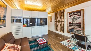 A modern kitchen with white cabinets and stainless steel appliances, a brown leather sofa, and a colorful rug. - Go2oporto A-Portoments (Porto)