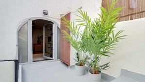 A narrow outdoor corridor with a white wall, a wooden door, and a potted plant. - Sweett | Verdi I - Two Bedroom Apartment, Sleeps 5 (Barcelona)