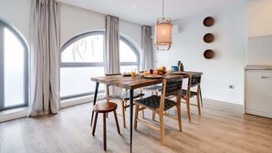 A modern dining area with a wooden table and chairs, a hanging light fixture, and large windows with curtains. - Sweett | Verdi I - Two Bedroom Apartment, Sleeps 5 (Barcelona)