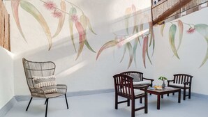 A room with a high ceiling, a staircase, and a mural of hanging plants. There are three wooden chairs and a small table with a plant and a bowl of fruit. - Sweett | Verdi I - Two Bedroom Apartment, Sleeps 5 (Barcelona)