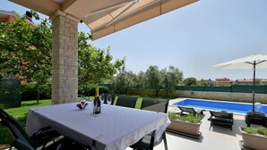 An outdoor patio with a table set for dining, a pool, and a view of the surrounding area.