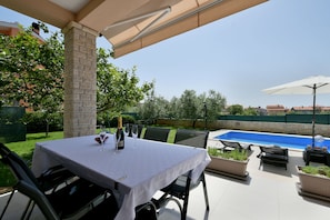 Une terrasse extérieure avec une table dressée pour les repas, une piscine et des chaises longues.