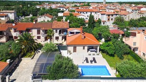 A residential area with a swimming pool, surrounded by houses with red-tiled roofs and a prominent church tower in the background.
