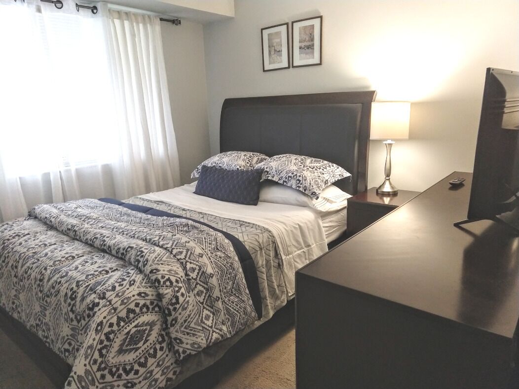 A hotel room with a bed, a bedside table with a lamp, a TV, and a window with curtains.