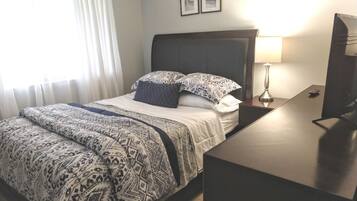 A hotel room with a bed, a bedside table with a lamp, a TV, and a window with curtains.
