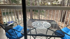 A metal table with a glass top and blue cushions on a balcony with a metal railing. - Inviting Condo in Central Raleigh (Raleigh)