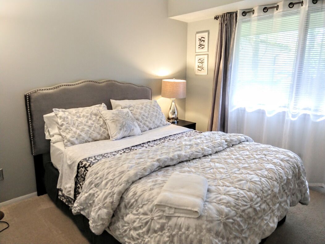 A neatly made bed with a patterned duvet, a bedside lamp, and curtains on a window.