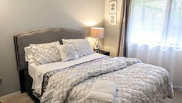 A neatly made bed with a patterned duvet, a bedside lamp, and curtains on a window.