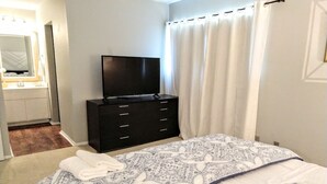 A bedroom with a bed, a TV on a dresser, a bathroom with a mirror, and a curtain. - Inviting Condo in Central Raleigh (Raleigh)