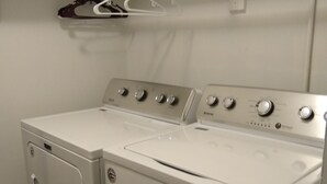 A laundry area with a front-loading washer and dryer, a drying rack, and a control panel with multiple settings. - Inviting Condo in Central Raleigh (Raleigh)