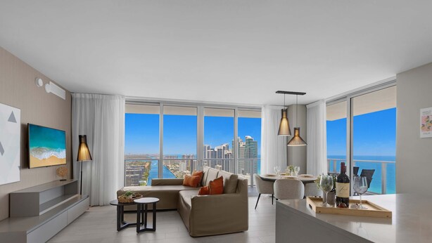 A modern living room with a large window, a sofa, a dining area, and a TV on the wall. - Luxury 2Br- Front Ocean & Bay View|  Amazing Pools (Hollywood)