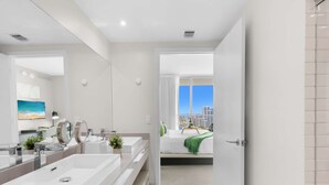 A modern bathroom with a large mirror, dual sinks, and a view of a cityscape through an open door. - Luxury 2Br- Front Ocean & Bay View|  Amazing Pools (Hollywood)