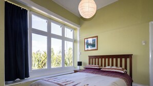 A bedroom with a large window, a bed with patterned bedding, a wooden headboard, and a wall-mounted picture. - Oroua Cottage - Rangataua Bach (Ohakune)