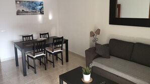 A living room with a dining table, chairs, a sofa, a coffee table with a plant, a wall-mounted lamp, and a painting. - Apartment on the beach in Rincón de la Victoria. (Rincón de la Victoria)