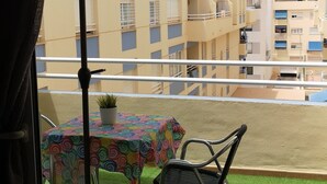 A balcony with a table and chairs, a green umbrella, and a view of buildings in the background. - Apartment on the beach in Rincón de la Victoria. (Rincón de la Victoria)