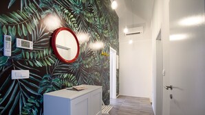Ein Flur mit Wandbild von grünen Blättern, einem weißen Schrank, einem Spiegel mit rotem Rahmen und einer Tür zu einem anderen Raum.