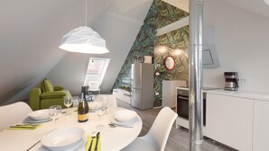 Eine moderne Küche mit weißen Schränken, ein Essbereich mit rundem Tisch und weißen Stühlen sowie eine Wand in Grüntönen.