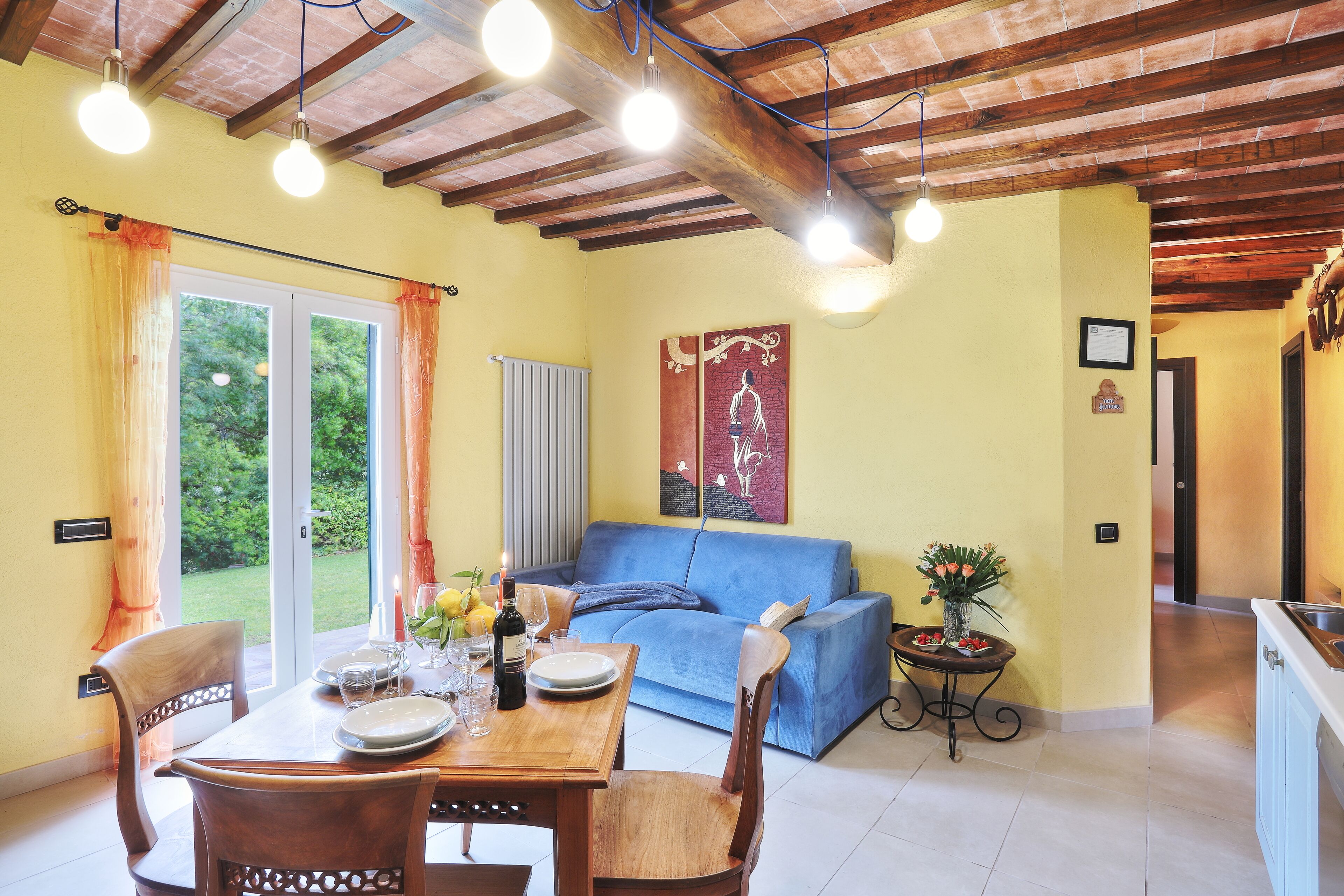 Zona pranzo con tavolo apparecchiato per quattro, divano blu e cucina sullo sfondo.