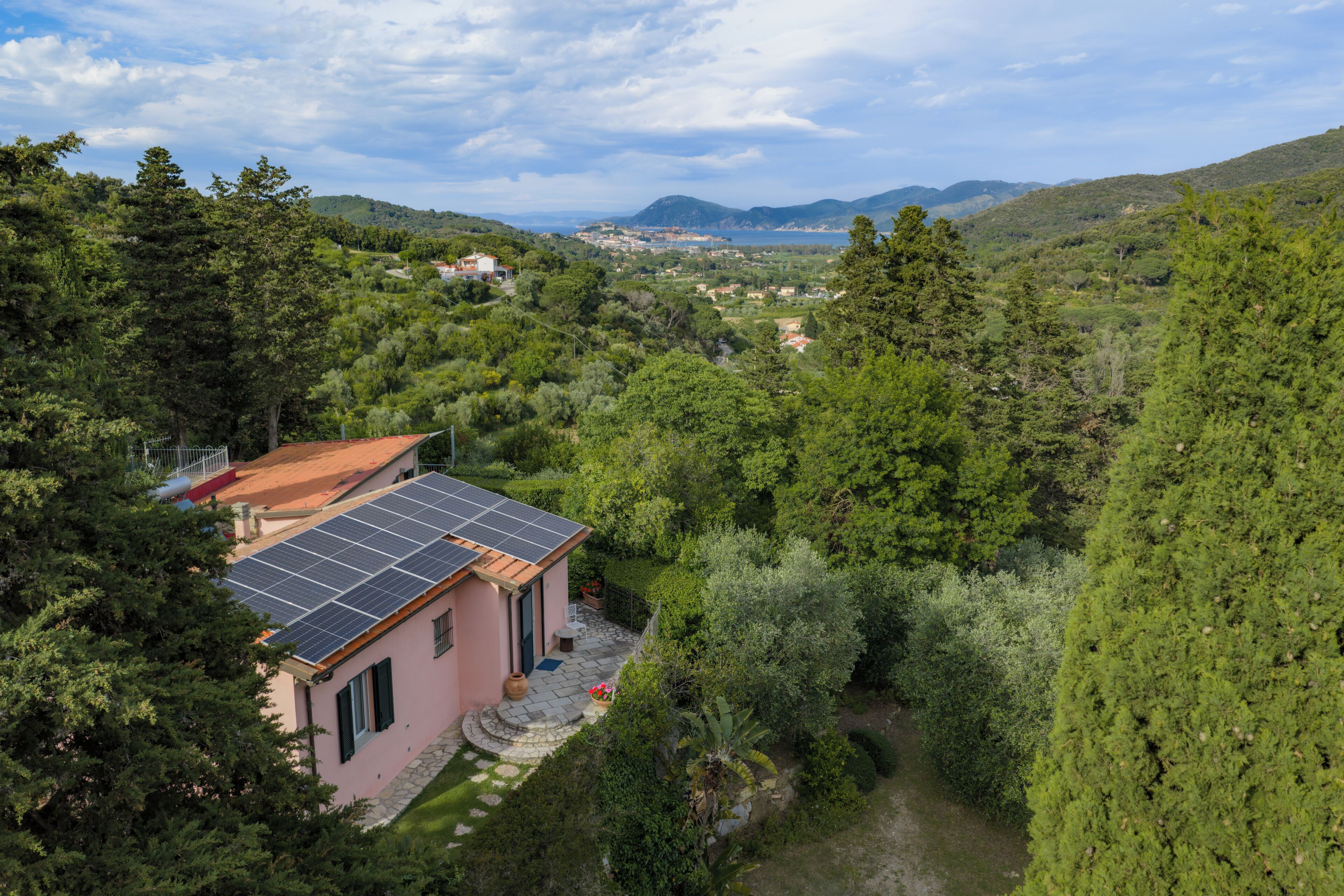 Ein Haus mit Solardach, umgeben von üppigem Grün und Hügeln im Hintergrund.
