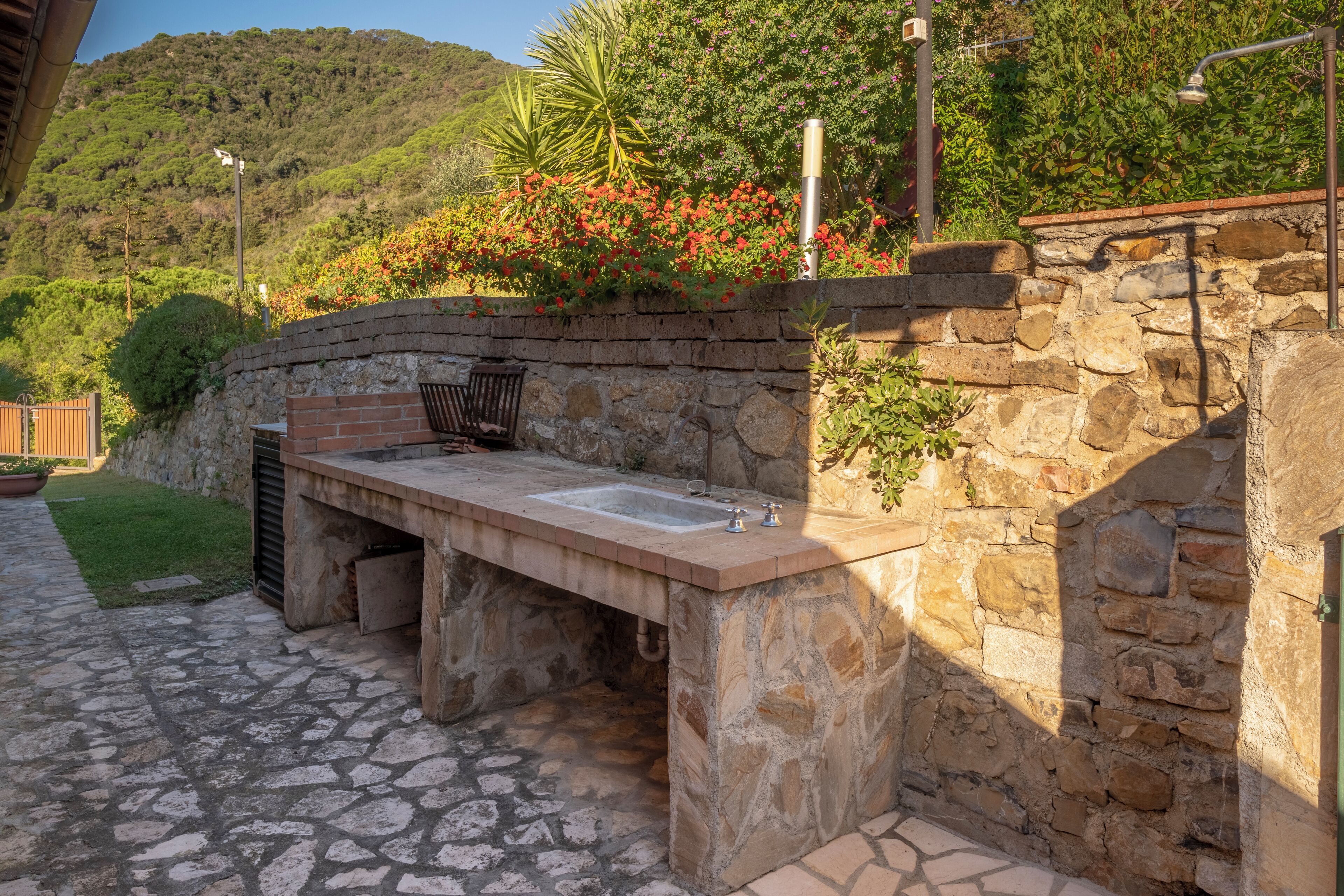 An outdoor kitchen area with stone walls, a sink, and a grill.