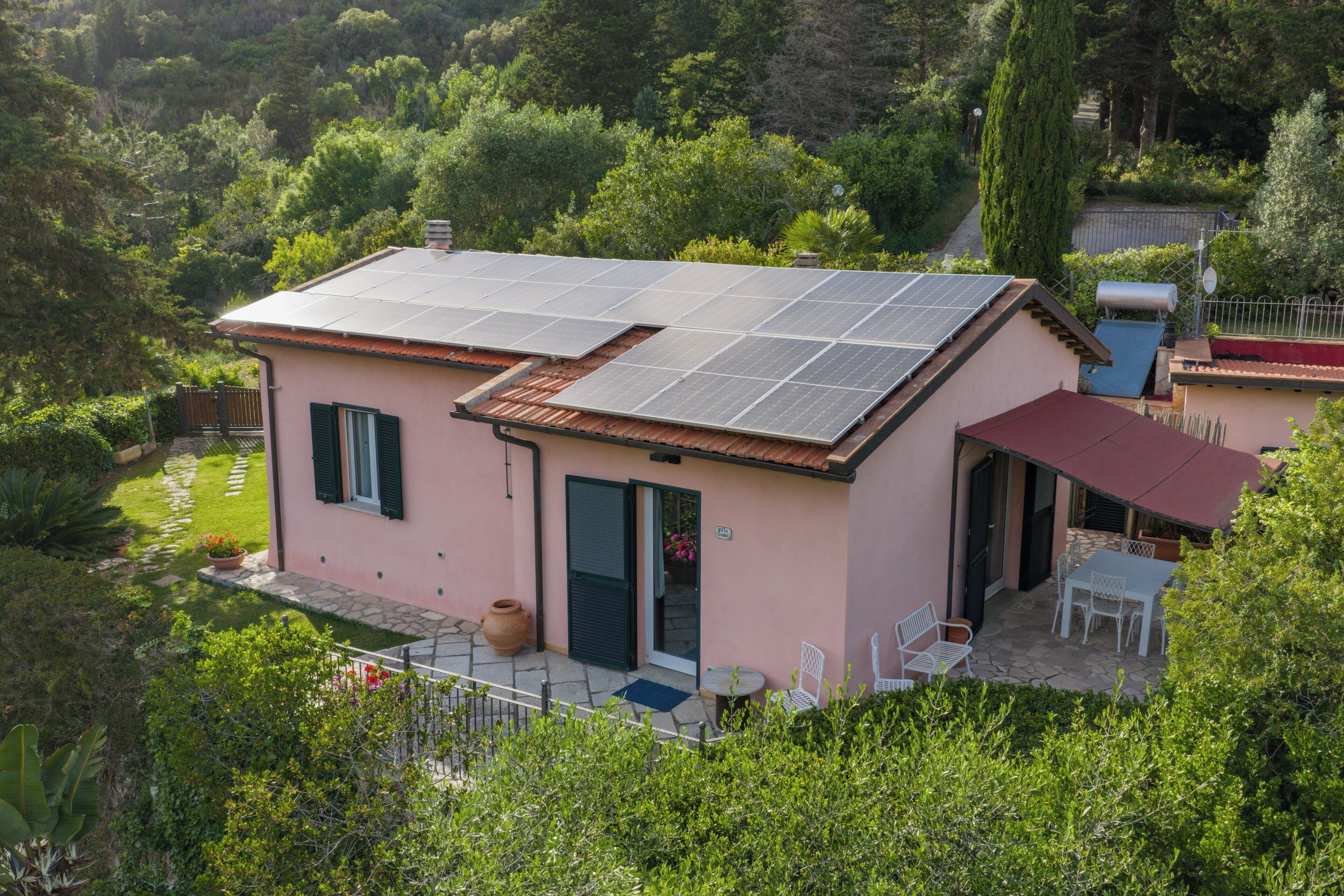 Una casa rosa con paneles solares, un patio con mobiliario exterior y un jardín.