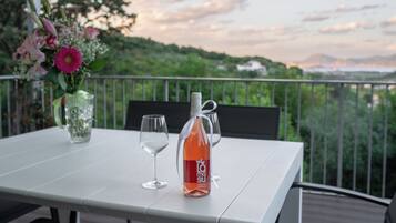 Une table avec une bouteille de vin, un verre et un vase de fleurs, placée sur un balcon donnant sur un paysage magnifique.