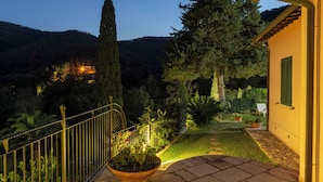 Un jardin bien éclairé, avec un chemin de pierre menant à une maison aux volets verts.