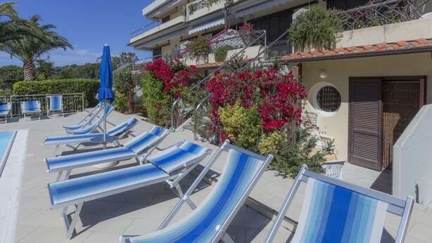 A poolside area with sun loungers and a blue umbrella. - Il Porto Monolocale 4 (Porto Azzurro)