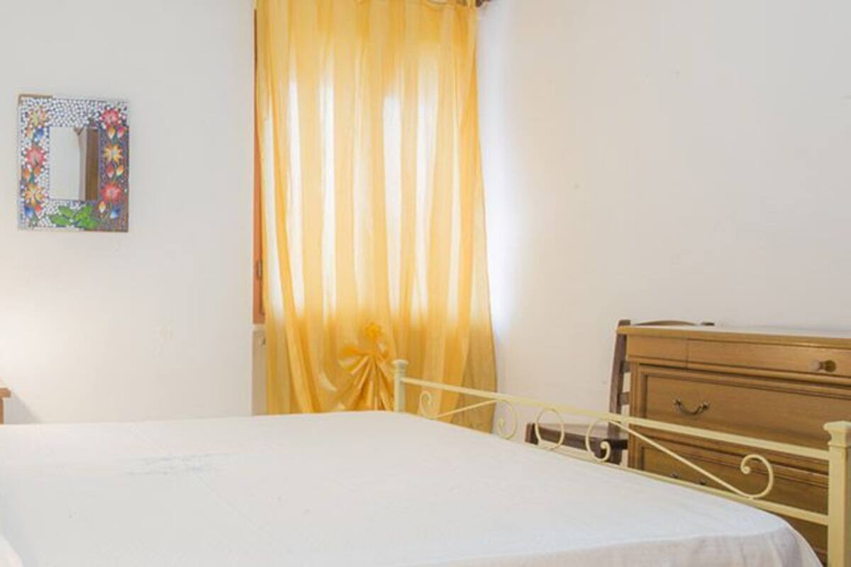 A bedroom with a bed, a nightstand, a dresser, a mirror, and a window with curtains.