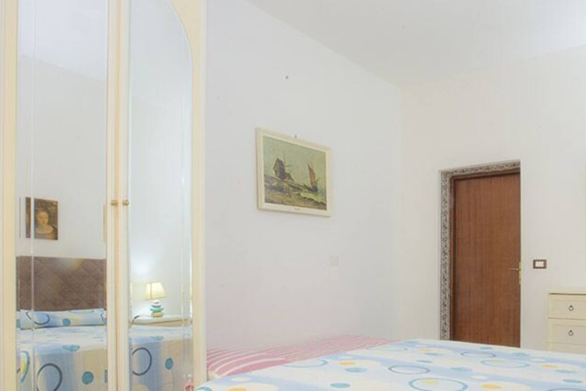 A bedroom with a bed, a dresser, a mirror, a door, and a window with curtains.