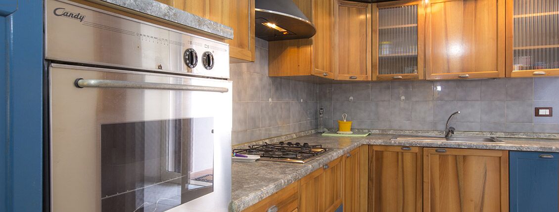 A kitchen with a Candy brand oven, wooden cabinets, granite countertops, and a stainless steel sink.